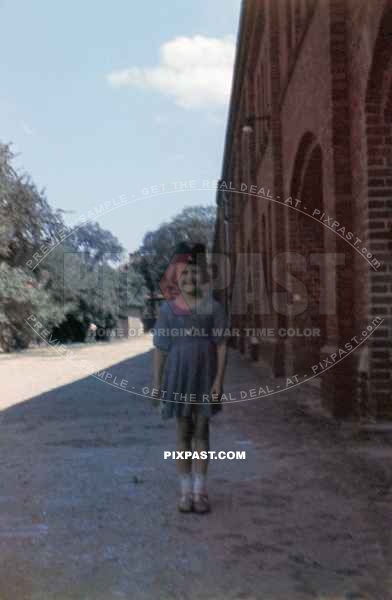 Daughter of a German soldier wearing her dads overseas cap beside a army horse stables. Near Berlin Germany 1940