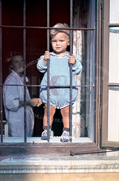 Young boy holding the metal bars on the window. With his mother looking on from behind. Austria 1939